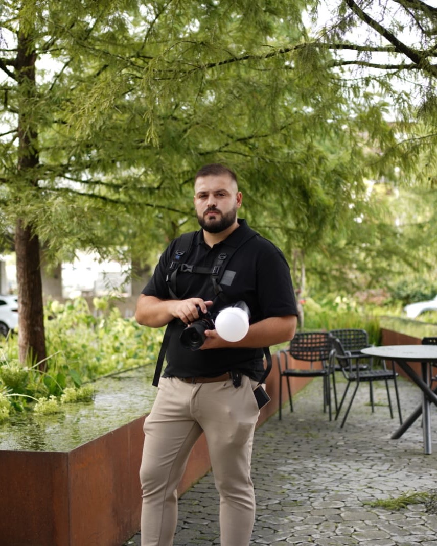 Edis Kadiric steht mit Kamera und Blitz unter Bäumen