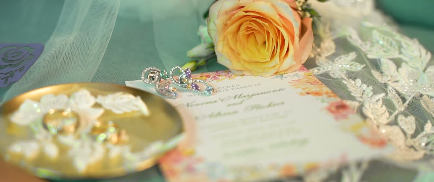 Ringe in einer goldenen Schale neben einer Rose und der Einladung