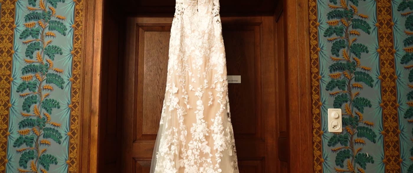 Brautkleid aus Spitze hängt vor einer Holztür