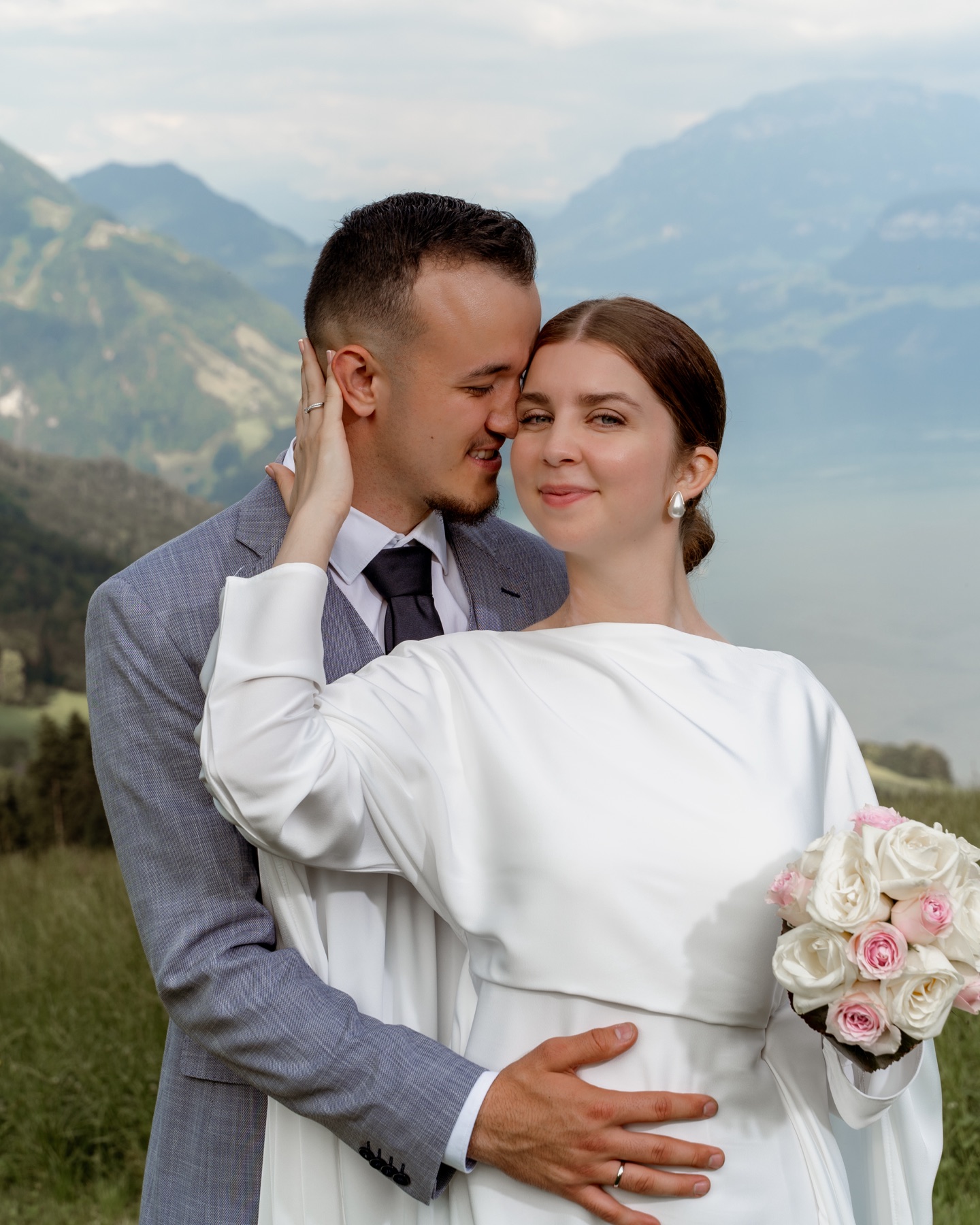 Brautpaar umarmt sich auf einer Bergwiese über dem See